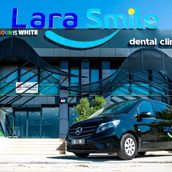 Exterior view of Lara Smile Dental Clinic in Antalya, Turkey, with a black transfer vehicle parked in front.